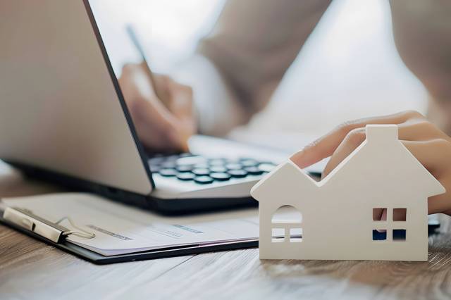 Foto: Person bearbeitet Akten, Modell eines Hauses im Vordergrund